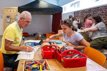 A young girl and an older person are sitting at a table drawing.