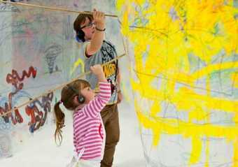 Two children with headphones on drawing on a surface with large implements