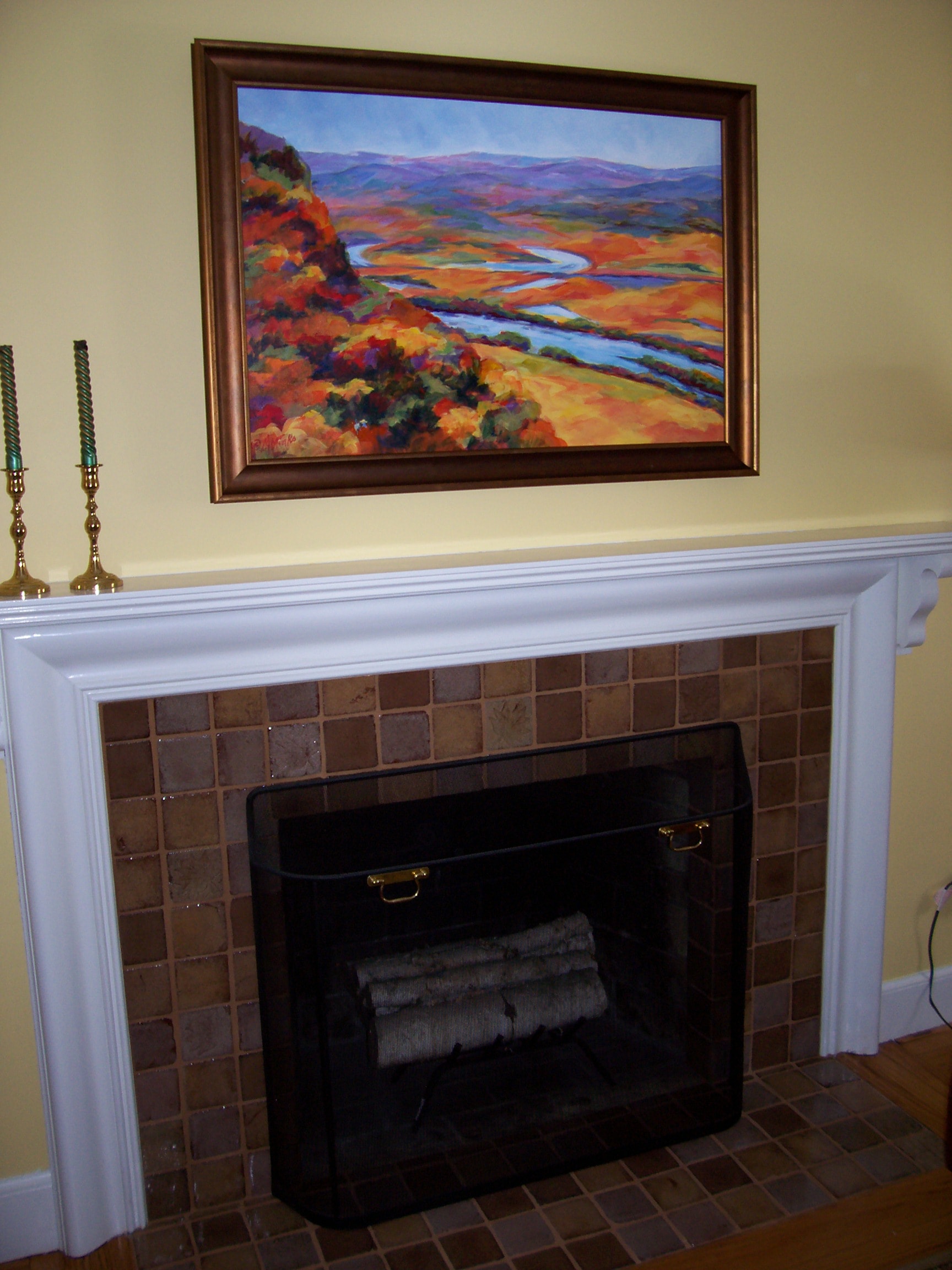 A painting of an aerial view of a river winding through a hilly autumn landscape above a fireplace