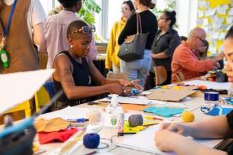 A person with a shaved head is creating something with their hands on a table surrounded by young people