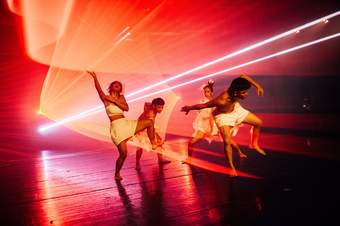 Four people dancing in front of orange lights