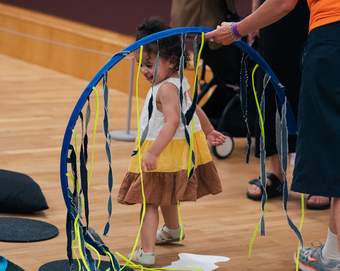 A young child looks around at an arc with dangling ribbons, in a gallery space