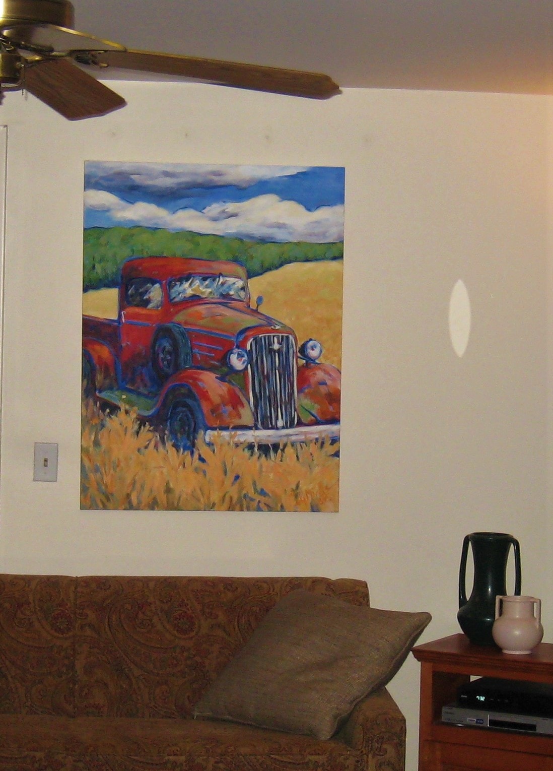 A painting of a red truck in a field displayed over a couch in a home