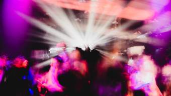 Purple, blue and pink lights blur an audience filled of people inside a club