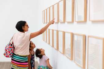 A parent points out details in framed artworks to two children