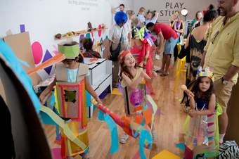 Three kids dressed in DIY costumes are playing, the rest of Play Studio is filled with adults and children creating other costumes