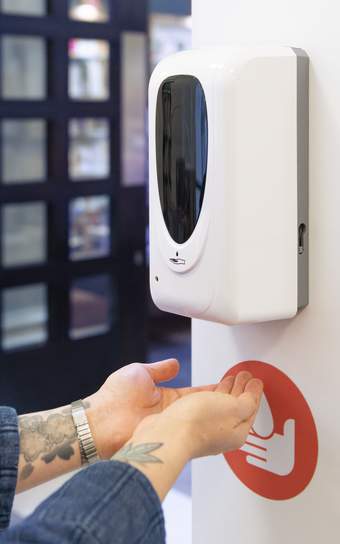 Hands beneath a hand sanitiser sensor