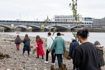 8 people walking along the Thames riverbank towards Blackfriars bridge, some holding branches